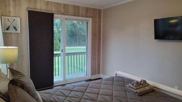 Une chambre avec un grand lit, une porte-fenêtre coulissante donnant sur un balcon, un téléviseur fixé au mur et une lampe sur une table de chevet.