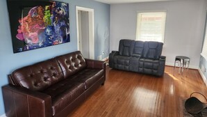 A living room with a brown leather sofa, a gray sofa, a large abstract painting, and a window with blinds. - 3bd Family-sized house, 5 minutes to National park, 12 minutes to the Capital. (Washington)