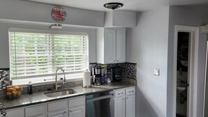 A modern kitchen with white cabinets, a granite countertop, a built-in dishwasher, and a window with blinds. - 3bd Family-sized house, 5 minutes to National park, 12 minutes to the Capital. (Washington)