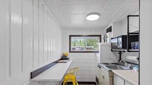A compact kitchen with white cabinetry, a built-in stove, a sink, and a window providing a view of the outdoors. - Relax at Lazy Duck Inn #18: a 2BR suite with kitchenette, just 1 minute to Yellowstone. (West Yellowstone)