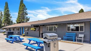 A motel with a barbecue grill, blue picnic tables, and a bench. - Relax at Lazy Duck Inn #18: a 2BR suite with kitchenette, just 1 minute to Yellowstone. (West Yellowstone)