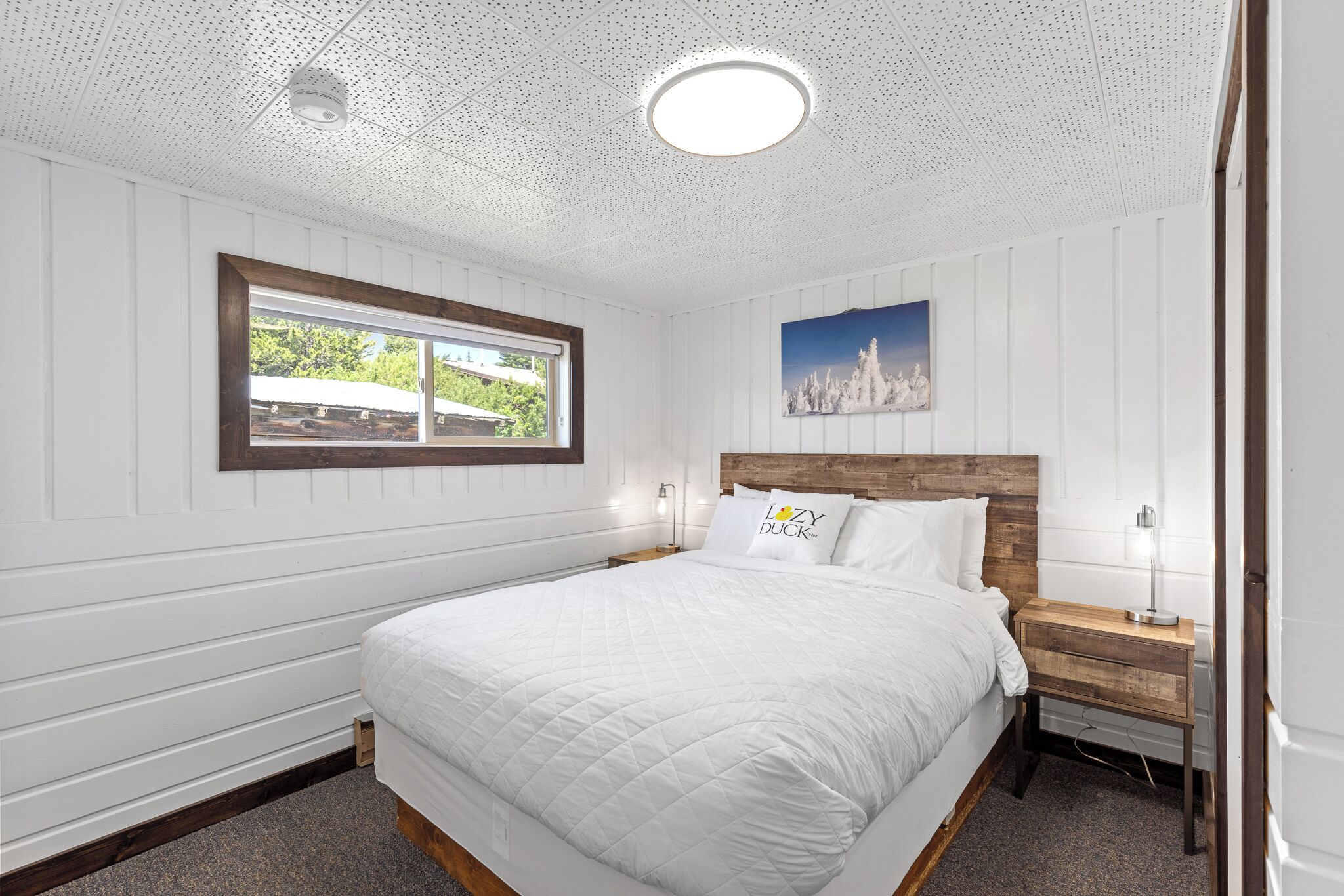 A bedroom with a large bed, wooden headboard, a window with a view, and a painting on the wall.