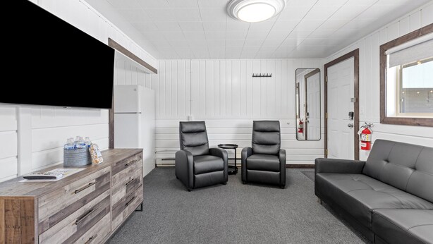 Una habitación con un aparador de madera, dos sillas de cuero negro, un sofá gris, una mesita y un techo blanco con una lámpara.