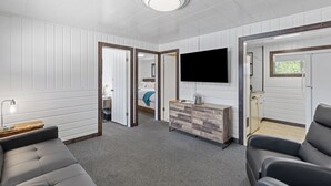 Una sala de estar moderna con un sofá gris, una mesa de centro de madera, un televisor montado en la pared y un mueble de madera.