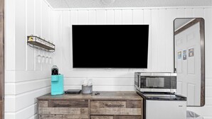 A compact kitchen with a flat-screen TV, a microwave, and a coffee maker on a wooden cabinet. - Stay at Lazy Duck Inn #20 Double Queens, just 1 minute to Yellowstone! (West Yellowstone)