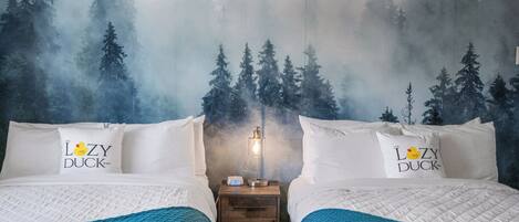 Une chambre d’hôtel avec deux lits, chacun agrémenté d’un oreiller orné du logo de « The Lazy Duck Inn », une table de chevet avec une lampe et une fresque murale sur le thème de la forêt.