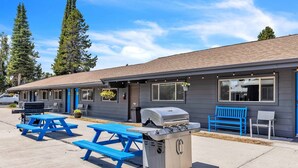 A motel with a barbecue grill, blue picnic tables, and a bench. - Cozy Lazy Duck Inn #22: 1 min to Yellowstone, 2 full beds, kitchen, sleeps 4! (West Yellowstone)
