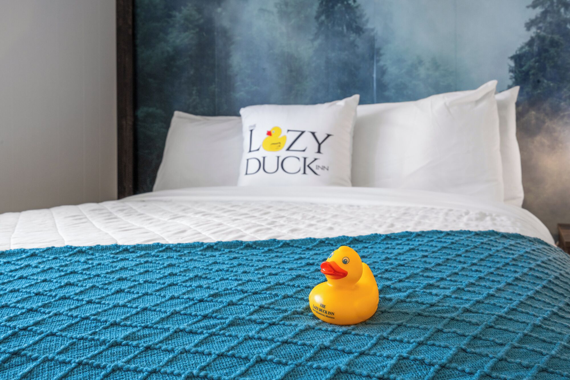 Un lit avec une couverture bleue tricotée et un oreiller orné du texte « LOZY DUCK INN ».