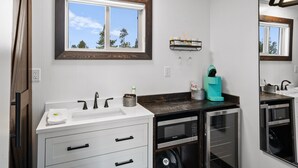 Un bagno moderno con uno specchio grande, una finestra con cornice in legno, un lavandino bianco e un forno a microonde incassato.