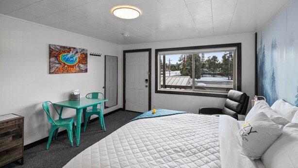 Una camera d'albergo con un letto, una scrivania, una sedia, una finestra vista alberi e un quadro appeso al muro.