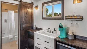 Ein Badezimmer mit Holztür, Waschbecken in Weiß, Spiegel und Fenster.