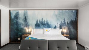 Ein Schlafzimmer mit einer großen Waldlandschaft als Wandbild, einem gesteppten Kopfteil, zwei Nachttischlampen und einem Kissen mit Entenmotiv.