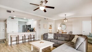 Amplia sala de estar con un sofá seccional grande, una mesa de centro de madera y una zona de cocina con un taburete de bar.
