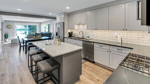 A modern kitchen with a central island, stainless steel appliances, and light gray cabinetry.