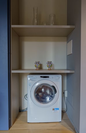 Compact laundry room with a front-loading washing machine and a shelf for storage.