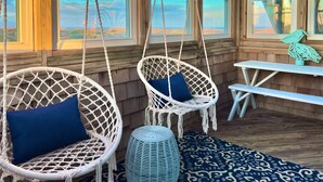 A cozy outdoor seating area with two white wicker chairs, a small round ottoman, and a wooden bench. - 7223- Pelican Watch - Oceanfront Salvo | Pool & Hot Tub | Sleeps 10 (Salvo)
