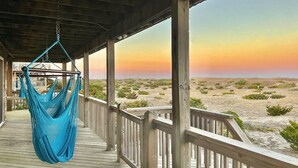 A hammock hanging on a wooden deck overlooking a desert landscape with a sunset. - 7223- Pelican Watch - Oceanfront Salvo | Pool & Hot Tub | Sleeps 10 (Salvo)