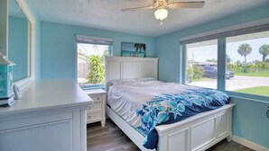 Une chambre à coucher comprenant un lit, une table de chevet, un ventilateur de plafond et une fenêtre donnant sur l’extérieur.