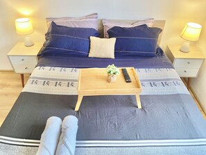 A neatly made bed with a dark blue and white patterned bedspread, two pillows, a bedside table with a lamp, and a tray with a remote control and a small plant. - Exclusive Panoramic Ocean View (1805) (Callao)