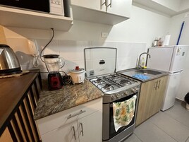 Una cocina con estufa a gas, licuadora, olla de cocción lenta, refrigerador y pileta.