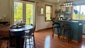 A spacious kitchen with a wooden island, bar stools, and a view of the outdoors through large windows. - Wildcat Cottage  (Port Angeles)