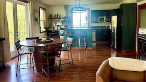 A spacious kitchen with a central island, wooden flooring, and a dining area with a round table and bar stools. - Wildcat Cottage  (Port Angeles)
