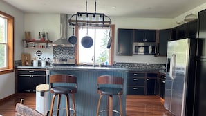 A modern kitchen with dark cabinetry, stainless steel appliances, and a central island with bar stools. - Wildcat Cottage  (Port Angeles)