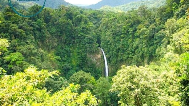 A lush green landscape with a waterfall and a logo for 'HOSPEDAJE PEÑA DEL Arenal'. - Hospedaje Peña del Arenal (La Fortuna)
