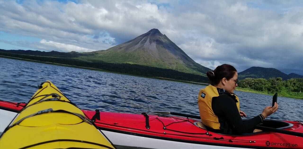 A person kayaking on a body of water with a mountain in the background.