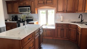Una cocina moderna con armarios de madera, una isla de mármol blanco, microondas integrado y un amplio ventanal que proporciona luz natural.