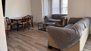 Una sala de estar con un sofá, una mesa de comedor y sillas, y un televisor.