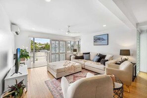 A modern living room with a sofa set, a coffee table, a TV, and a view through the glass door. - Sunsets at Snowmas Pooch Friendly Stunning Views (Noosa)