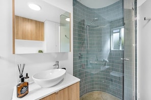 Une salle de bain moderne avec un lavabo blanc, des meubles en bois, une cabine de douche en verre et un grand miroir.