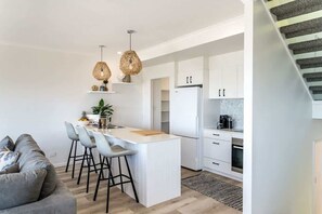 Cozinha moderna com armários brancos, uma ilha central com banquetas e uma escada à direita.
