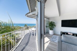 Ein Balkon mit Blick auf den Ozean, ein weißes Sofa, ein großer Topfpflanze und ein Flachbildfernseher.
