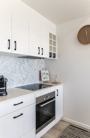 Eine moderne Küche mit weißen Schränken, einer Fischgräten-Spritzschutzwand, einem eingebauten Backofen und einer Uhr an der Wand.