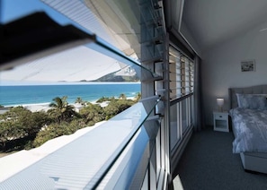 A balcony with a view of the ocean, a bed, and a nightstand.