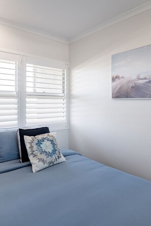 Un dormitorio con cama, ventana con persianas y un cuadro colgado en la pared.