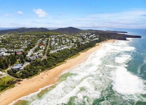 Vue aérienne d’une zone résidentielle côtière, avec des maisons, une plage et des vagues de l’océan.