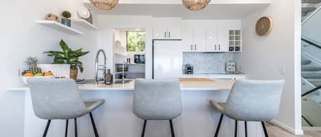Una cocina moderna con armarios blancos, una isla central con taburetes de bar, una lámpara colgante y un reloj en la pared.