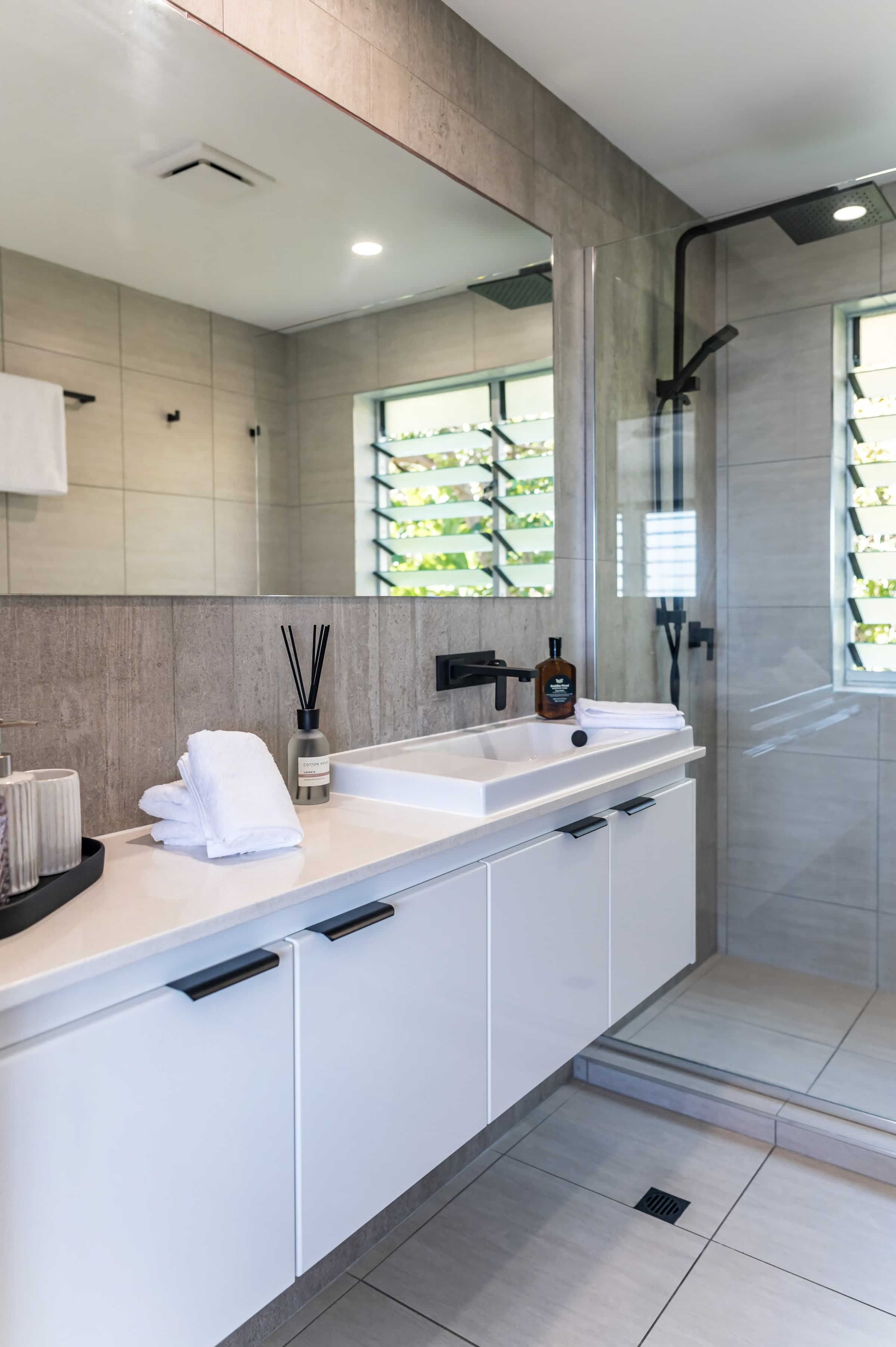 A modern bathroom with a large mirror, white cabinetry, and a shower area.