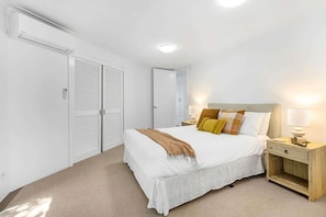 Une chambre à coucher avec un lit, des tables de chevet, une armoire et un luminaire au plafond.