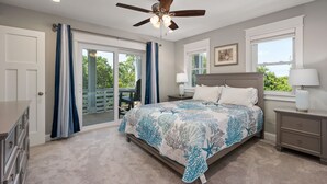 A bedroom with a bed, a ceiling fan, a nightstand, a lamp, a window, and a view of the outdoors. - Benders Beach Bungalow: New Construction, Golf Views, Elevator, Community Pool and Tennis Courts (Nags Head)