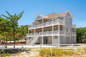 Una casa de playa de dos pisos con un balcón, una escalera y una valla blanca.