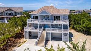 A two-story beachfront house with a balcony, a staircase, and a view of the ocean. - Benders Beach Bungalow: New Construction, Golf Views, Elevator, Community Pool and Tennis Courts (Nags Head)