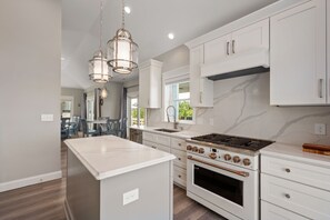 Una cocina moderna con armarios blancos, una isla central, electrodomésticos de acero inoxidable e iluminación colgante.