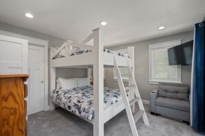 Una cama litera con escalera, un sofá gris, un televisor y un escritorio de madera en una habitación con paredes y alfombra grises.