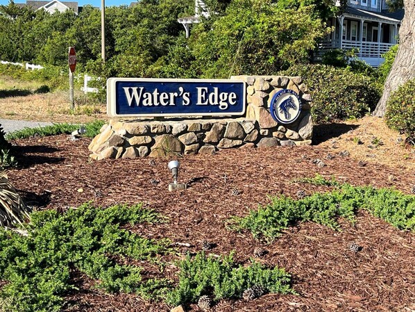 Un letrero que dice 'Water's Edge', con un muro de piedra y un emblema decorativo.