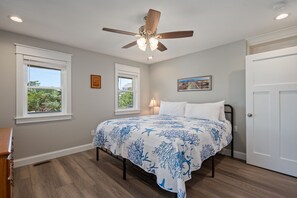 Un dormitorio con cama, ventilador de techo y dos ventanas.