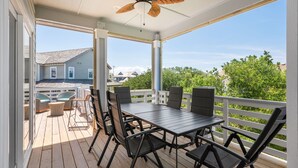 A covered outdoor deck with a table and chairs, a ceiling fan, and a view of neighboring houses and greenery. - Benders Beach Bungalow: New Construction, Golf Views, Elevator, Community Pool and Tennis Courts (Nags Head)